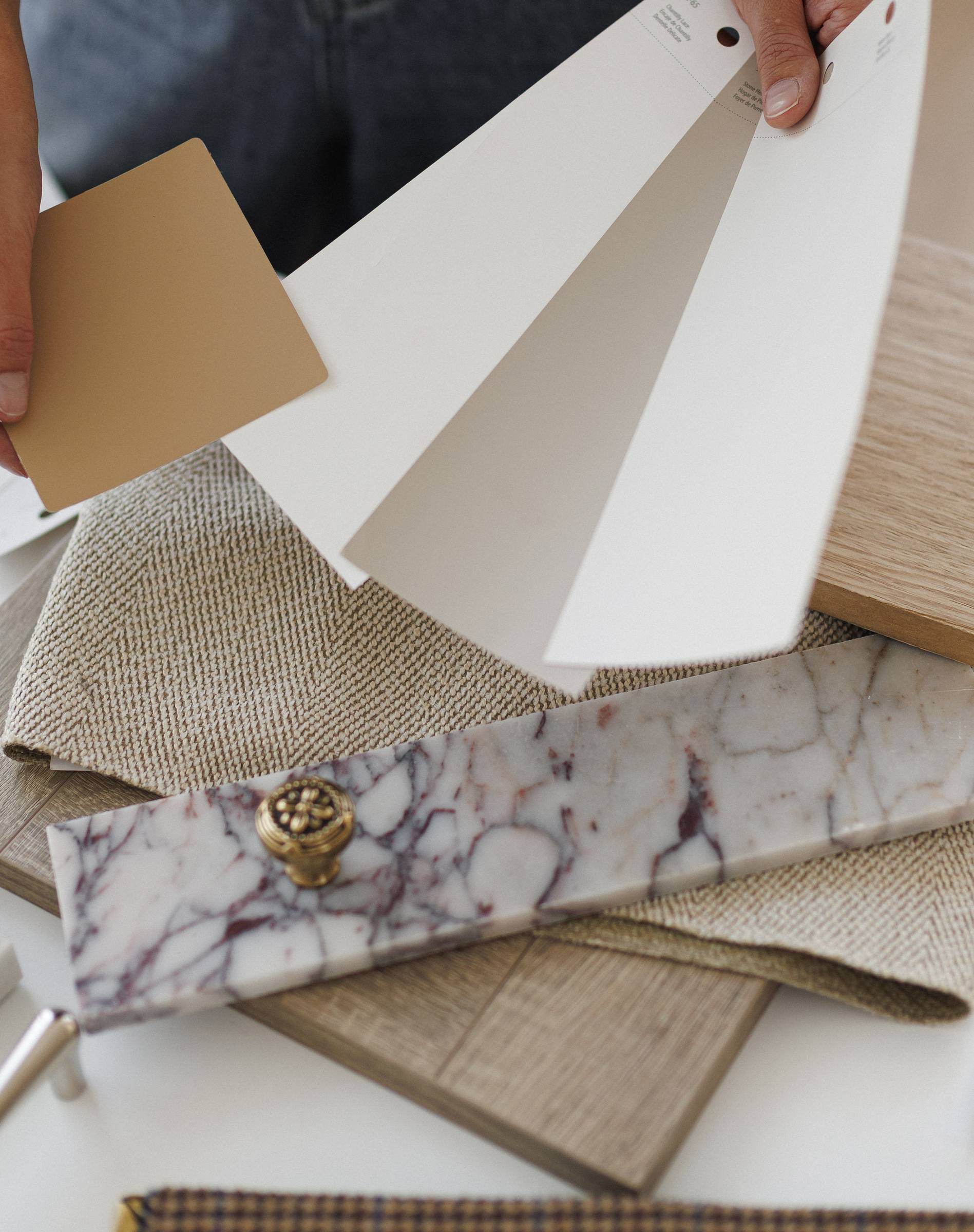 Paint swatches, oak and fabric samples, a marble tile and a brass knob on the design table