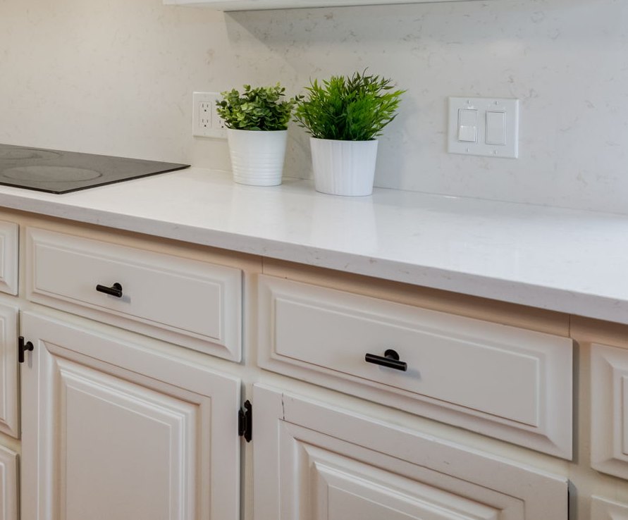 Painted white kitchen cabinets with black hardware and a quartz countertop